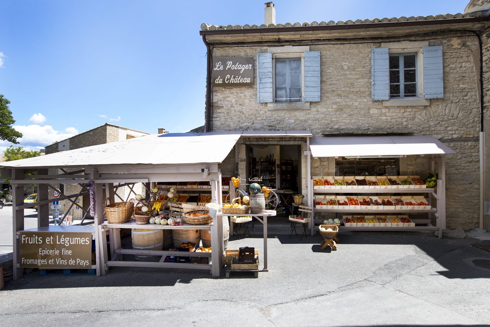 Le Potager du Château fruiterie in Gordes, with wooden produce displays of melons, tomatoes, peppers, and a sign reading Fruits et Légumes